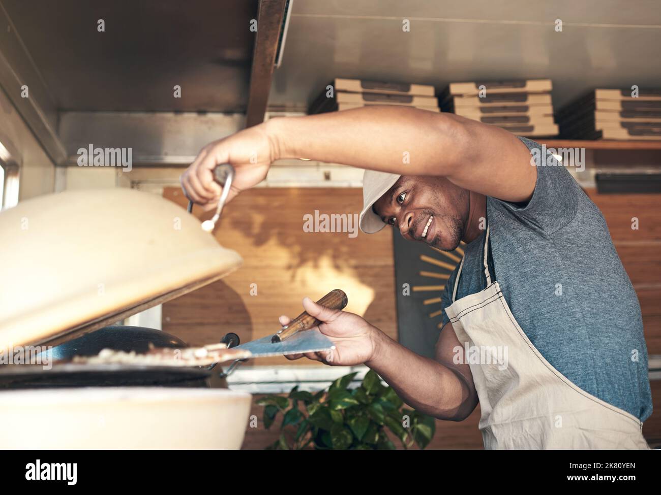 Lets get cooking. a handsome young man standing alone and putting a pizza in the oven at his restaurant. Stock Photo
