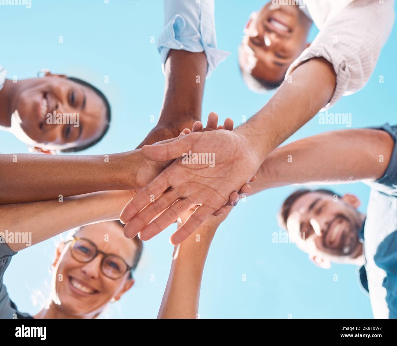Hands stacked, support and friends with motivation for collaboration, partnership and community with a blue sky. Low view of people with a goal Stock Photo