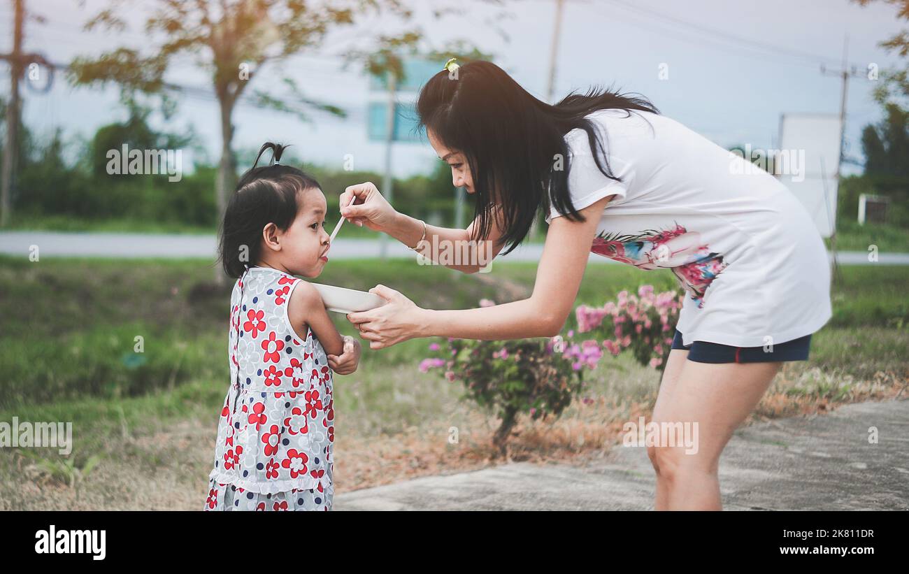 Mother feeding her daughter with a spoon. Mother giving food to her little girl child Stock Photo