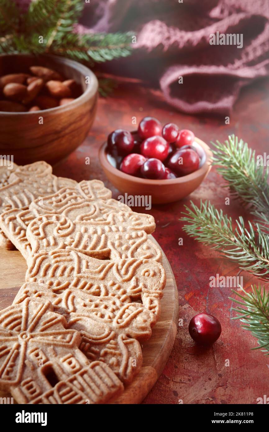 Speculoos or Spekulatius, Christmas biscuits, with cranberry berries, almonds on a table with kitchen towel and fir twigs. Traditional German sweets Stock Photo