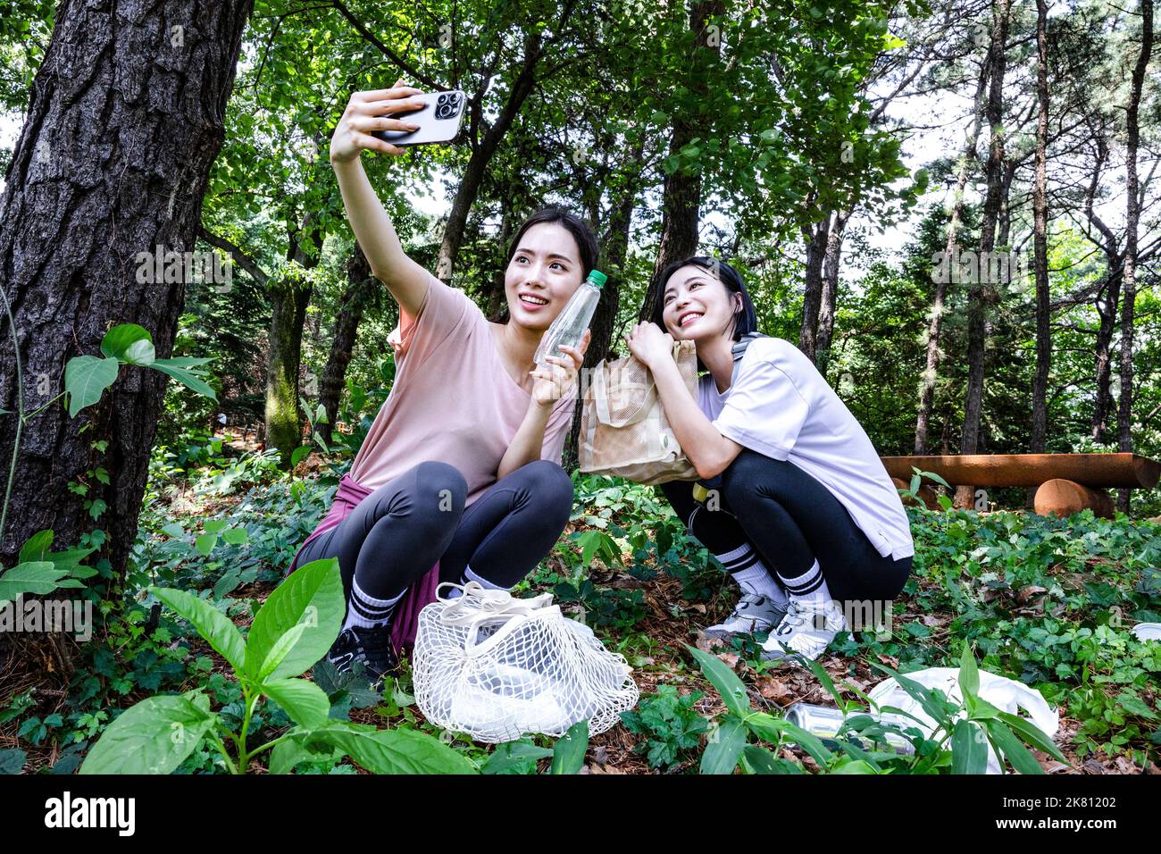 korean young woman hiking and plogging picking up litter, garbage with taking photo Stock Photo