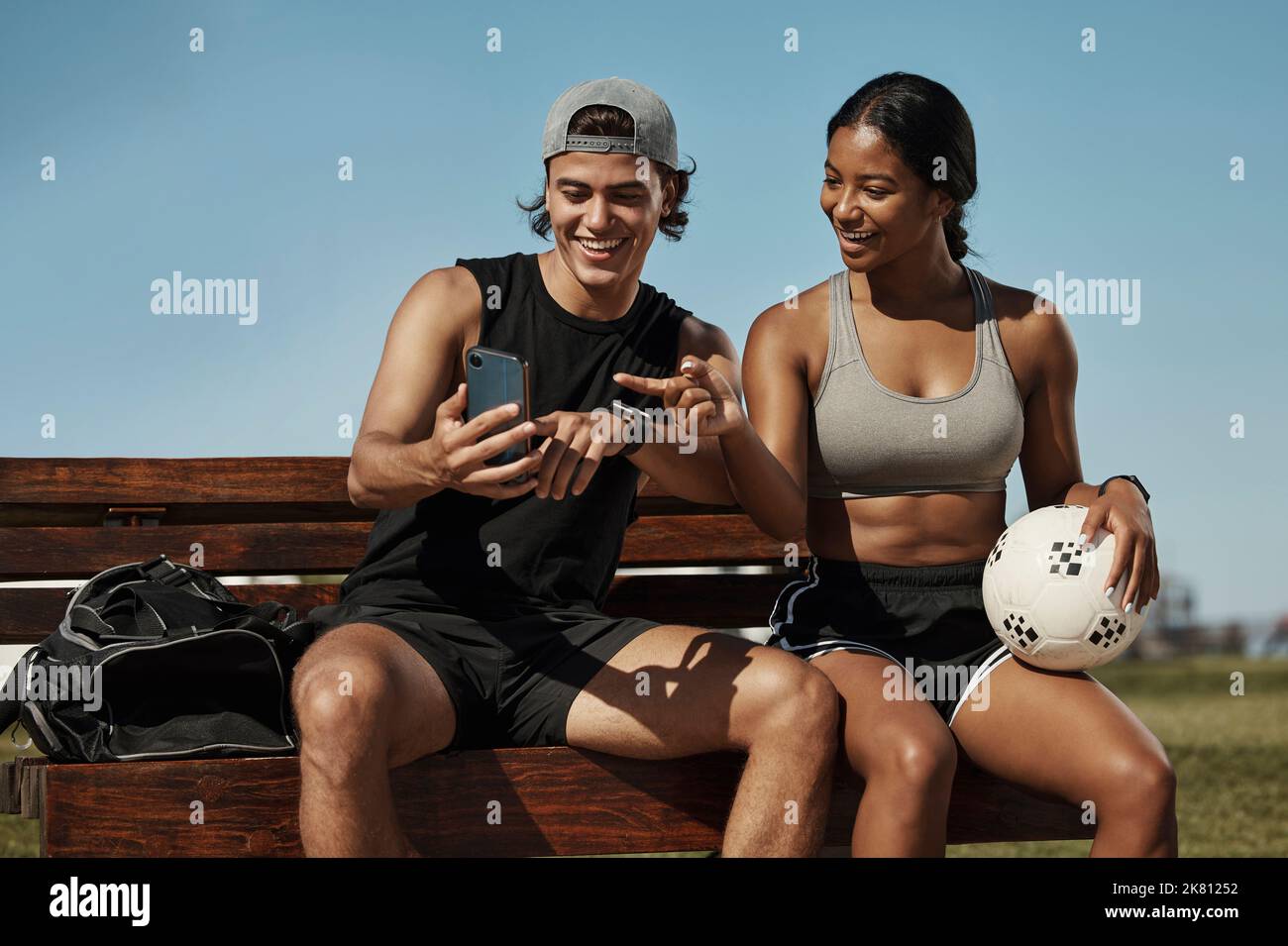 Sports friends, phone and relax while sitting in a park together, bond and laughing at social media post before morning cardio. Fitness, couple and Stock Photo