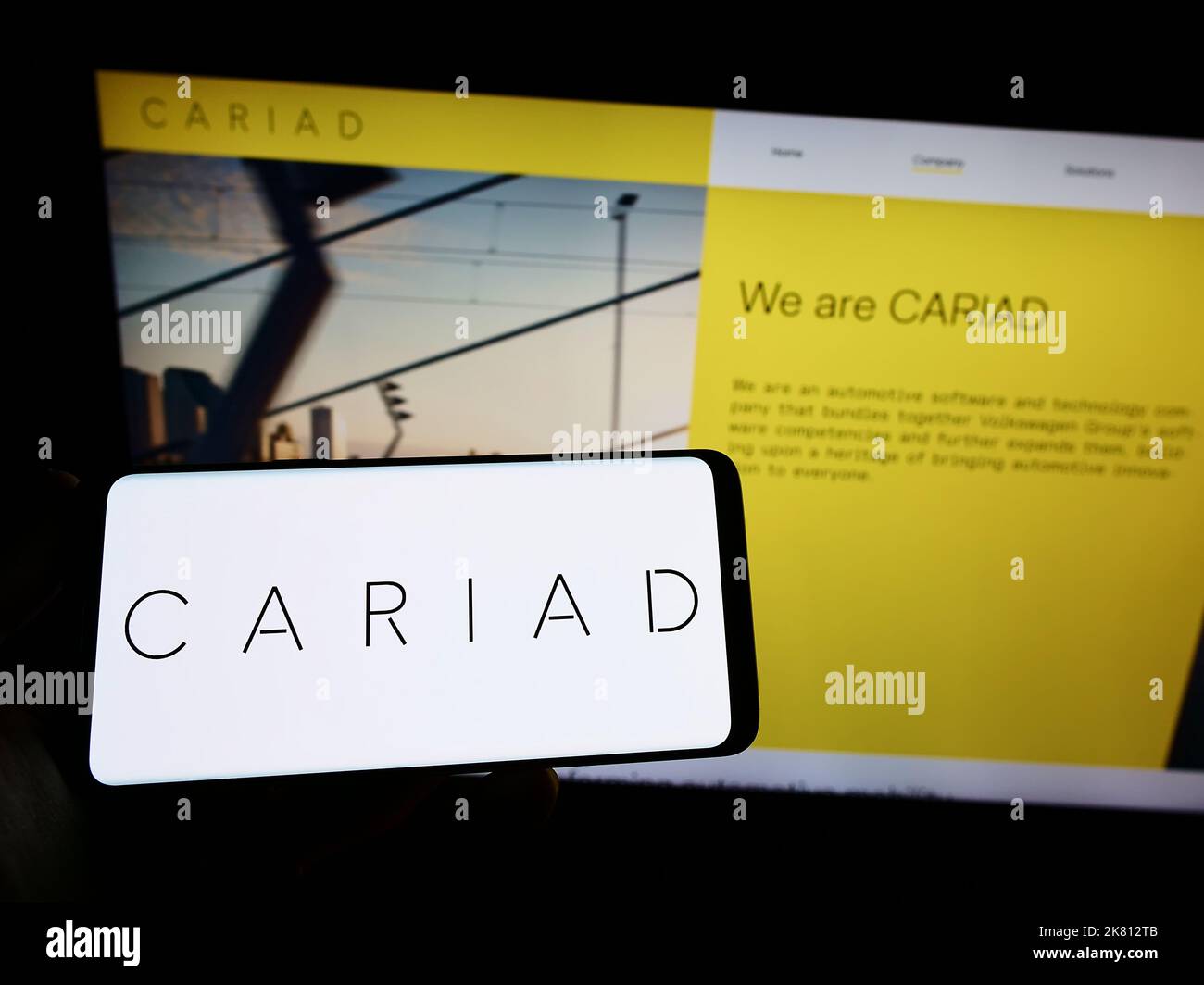Person holding smartphone with logo of German automotive software company Cariad SE on screen in front of website. Focus on phone display. Stock Photo