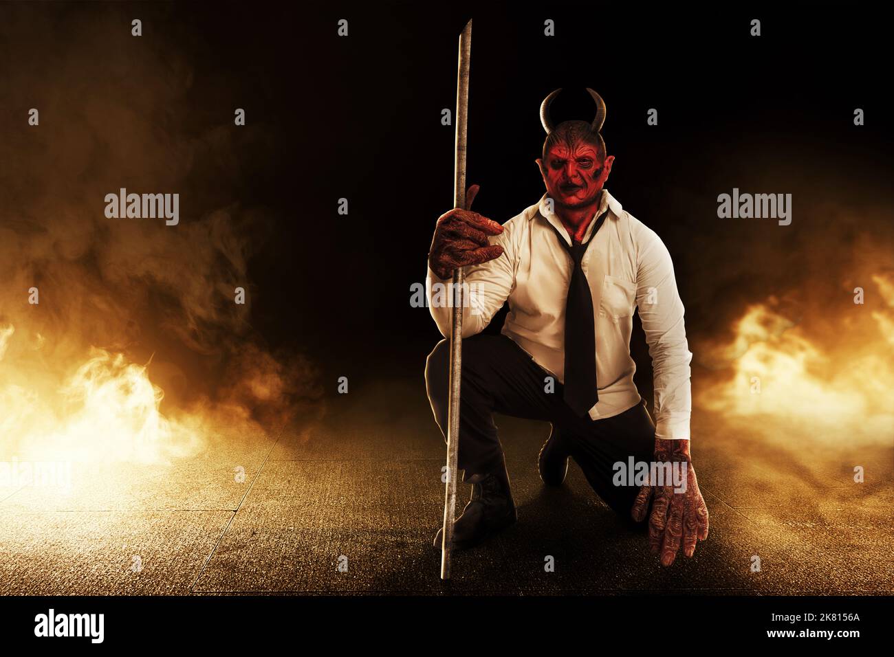 Devilman sitting while holding sticks with fire's background. Halloween concept Stock Photo