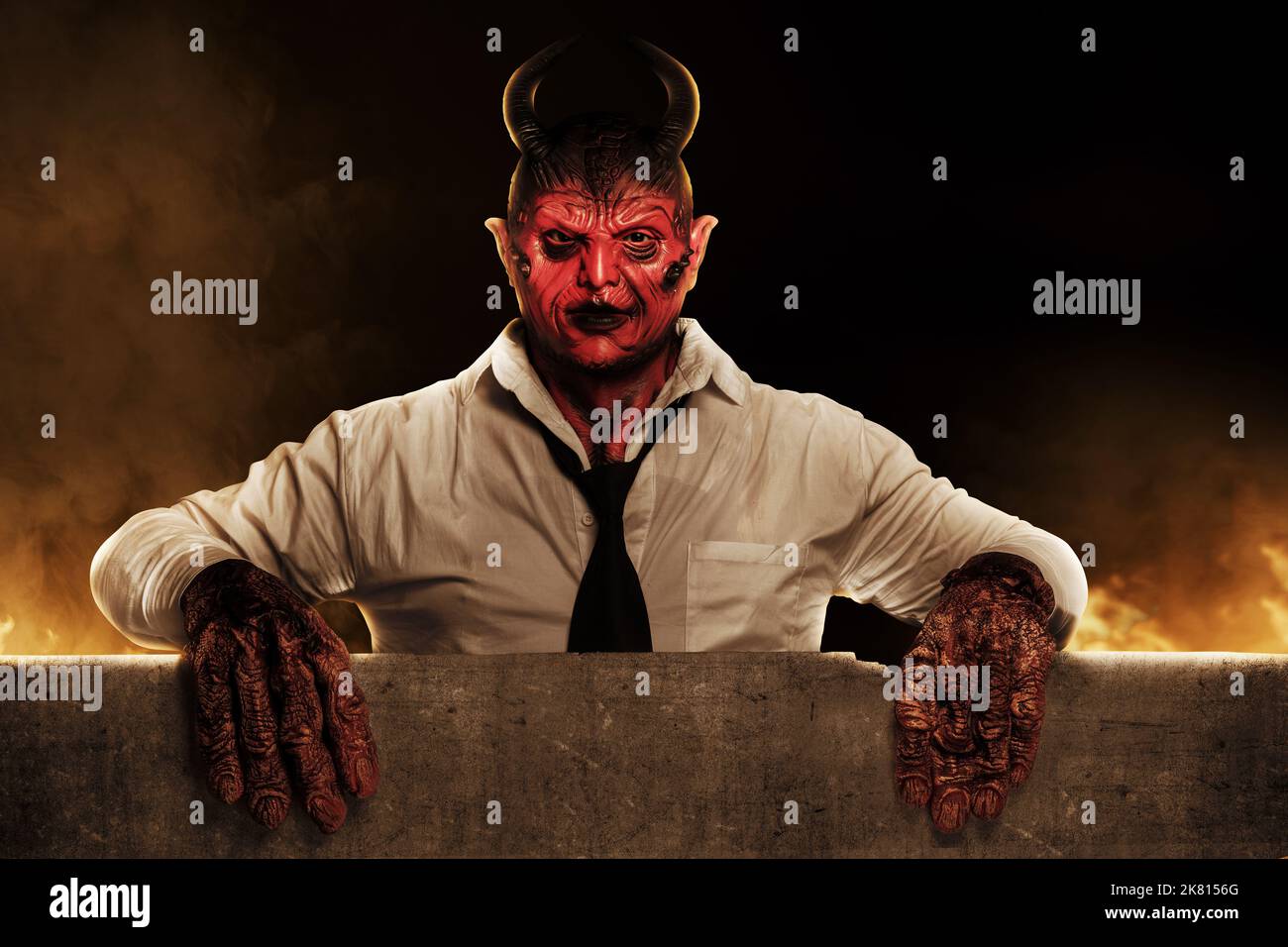 Devilman is standing behind the wall with the fire's background. Halloween concept Stock Photo
