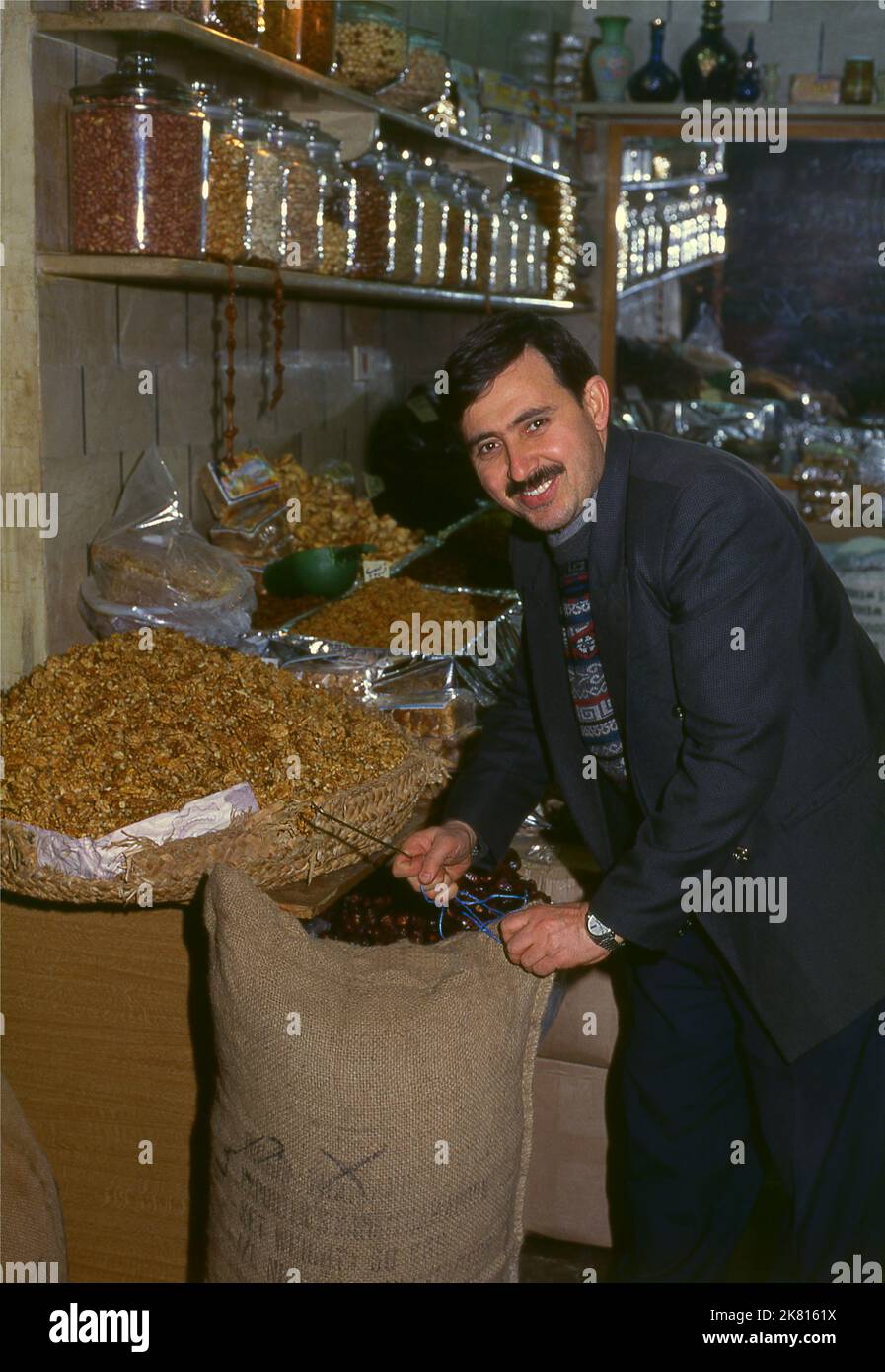 Syria: Nuts and dried fruit vendor in the ancient Great Bazaar, Aleppo (1997). Aleppo's Great Bazaar (in Arabic, suq or souq) was rebuilt first by the Egyptian Mamelukes who drove out the Mongols, and then, after 1516, by the Turks who incorporated Aleppo into the Ottoman Empire. During the Syrian Civil War, which started in 2011, Aleppo's historic suqs suffered serious damage.  Aleppo, the second city of Syria is possibly the longest continually inhabited settlement in the world. Its Arabic name, Halab, is mentioned in Semitic texts of the third millennium BCE. Stock Photo