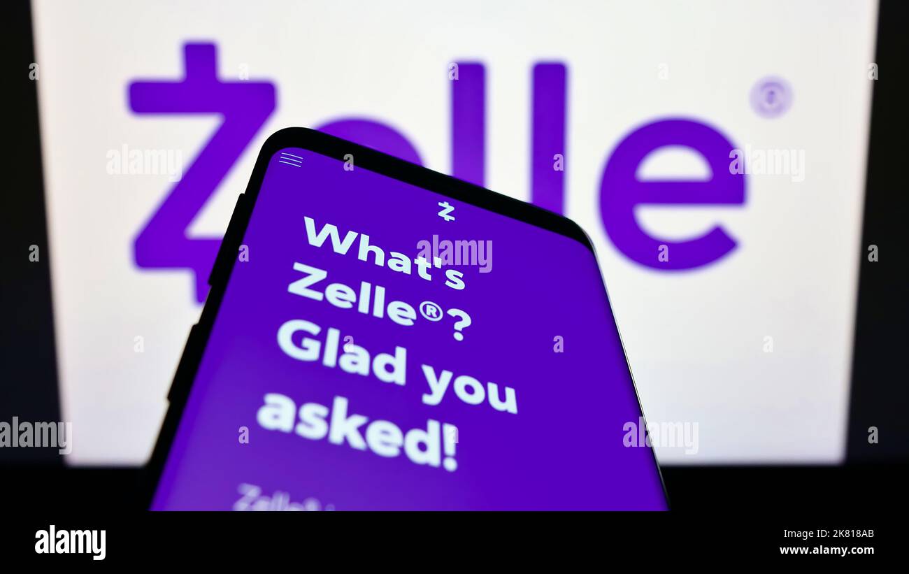 Smartphone with webpage of US digital payments company Zelle on screen in front of business logo. Focus on top-left of phone display. Stock Photo