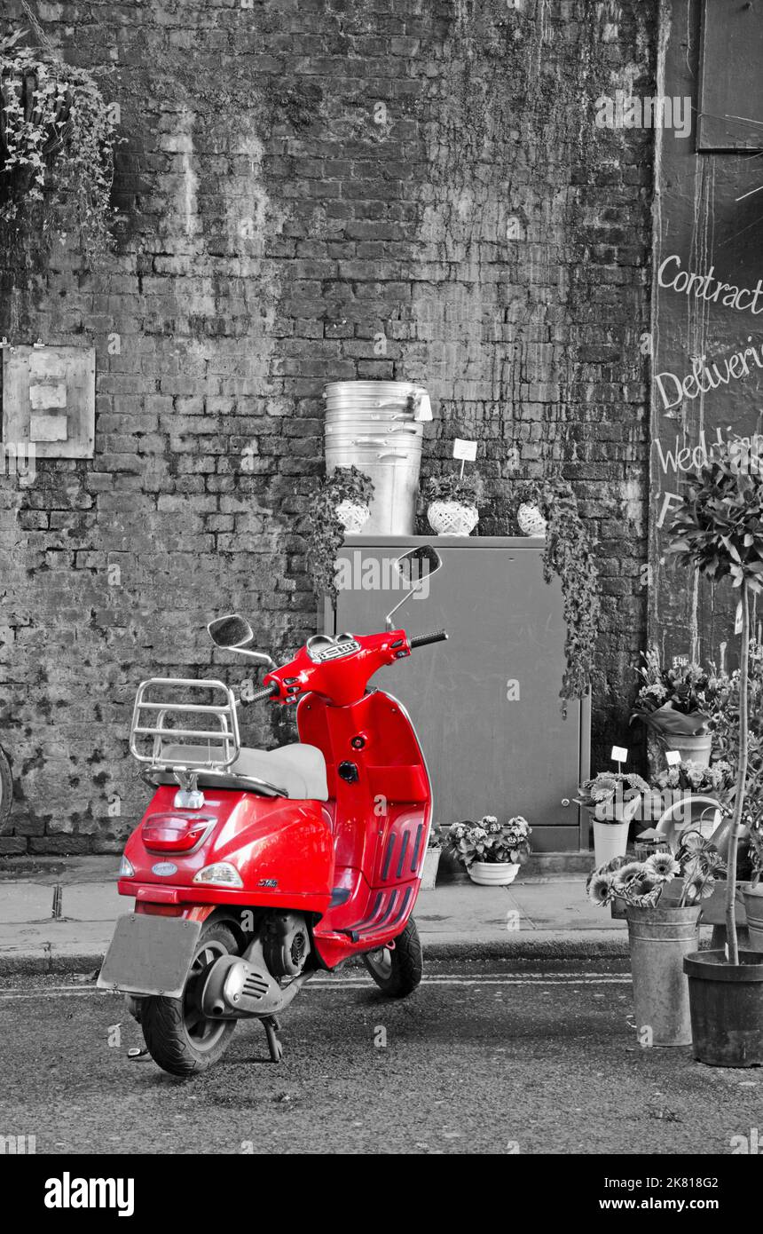 Red Vespa scooter parked in a street (monochrome background) Stock Photo