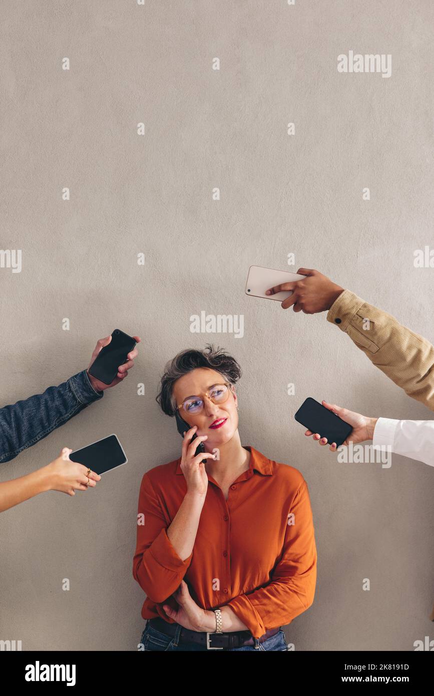 Mature businesswoman talking on the phone while surrounded by hands holding smartphones. Female business professional answering phone calls in a busy Stock Photo