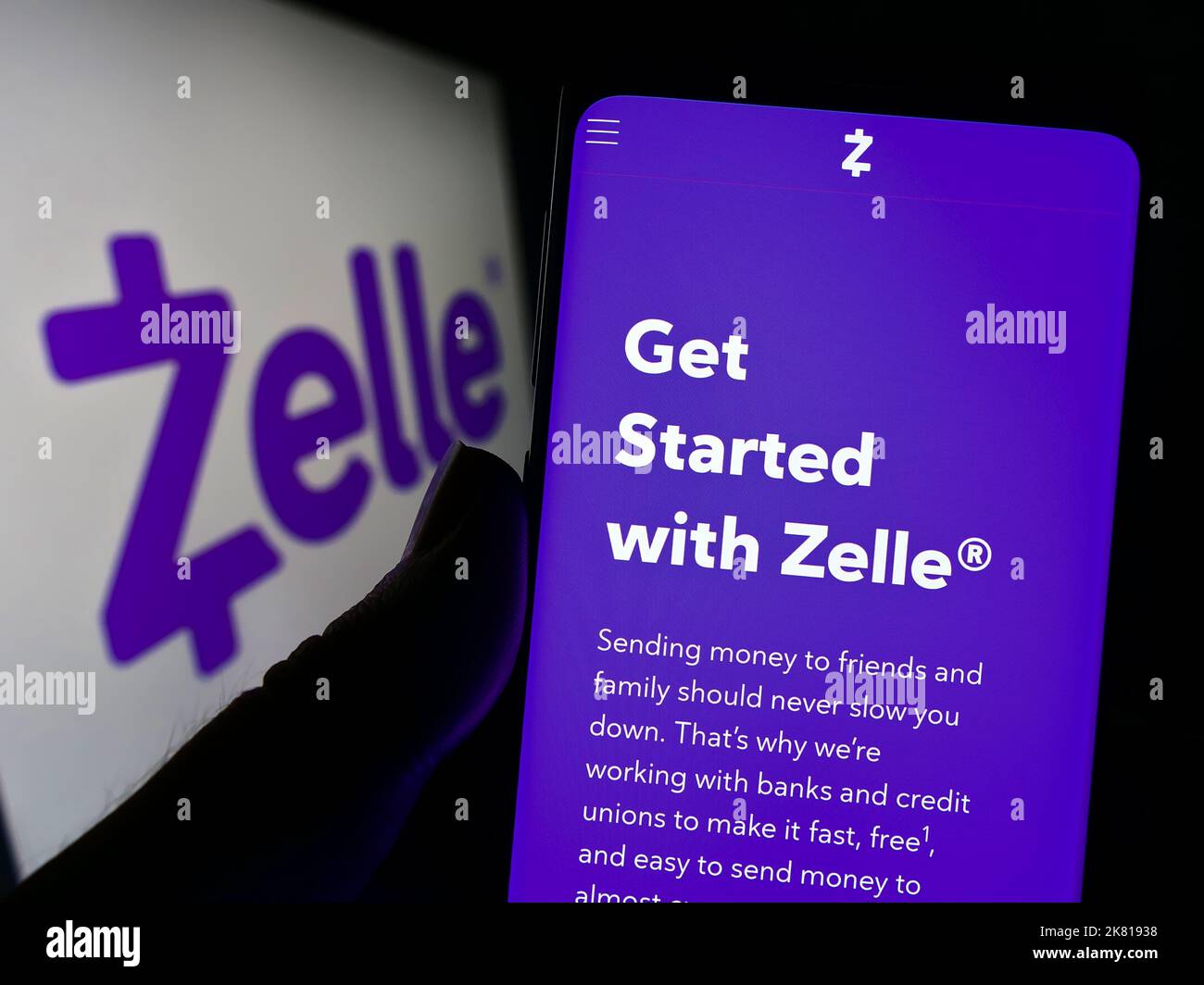 Person holding cellphone with website of US digital payments company Zelle on screen in front of business logo. Focus on center of phone display. Stock Photo