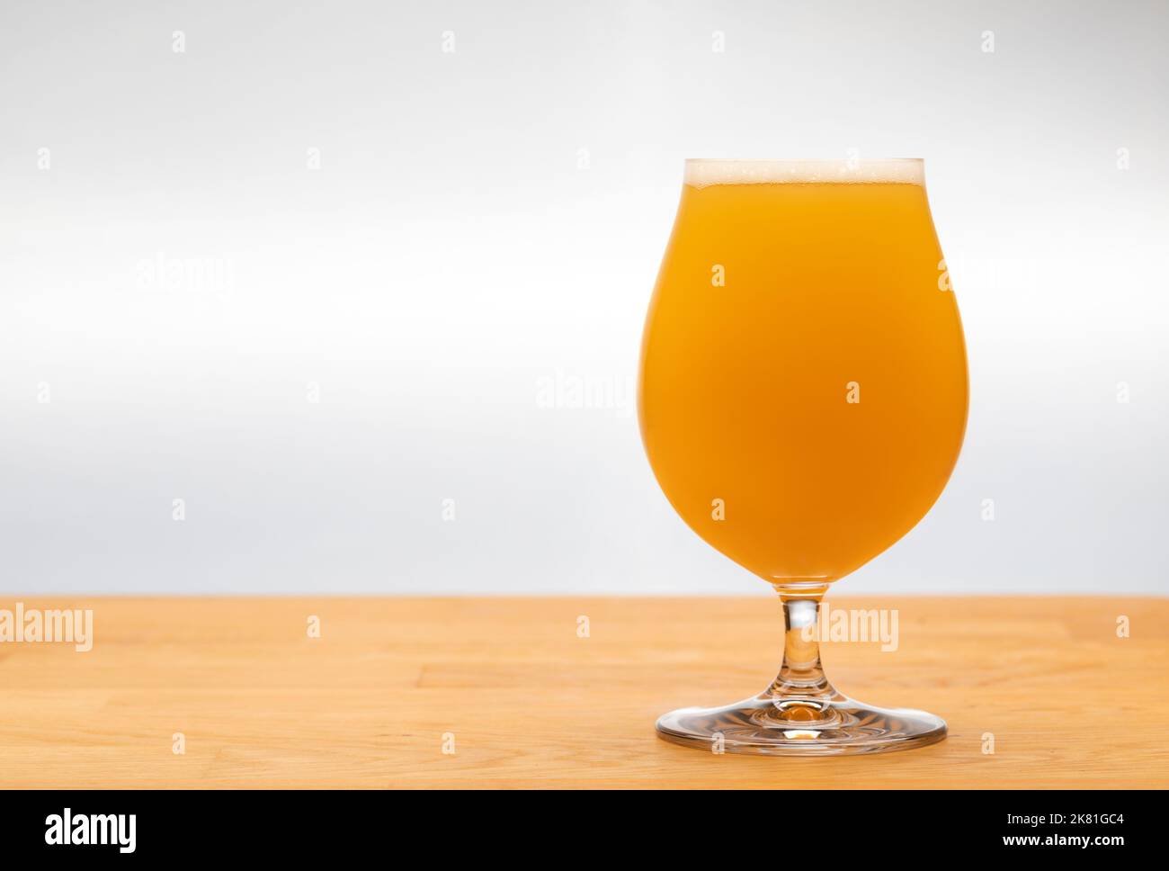 Full snifter glass of hazy New England IPA (NEIPA) pale ale beer on wooden table with grey background Stock Photo