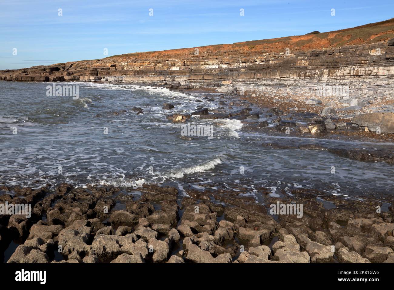 A large bay near the well-known Ogmore deeps showing rock layers and huge random rocks with the tide on the way in. Stock Photo
