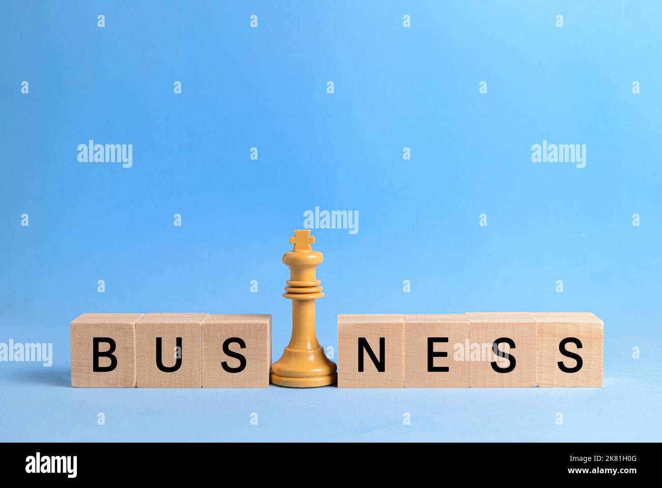 White chess king next to wooden blocks forming the word 'business', on blue background. Image to illustrate the concept of leadership and business str Stock Photo