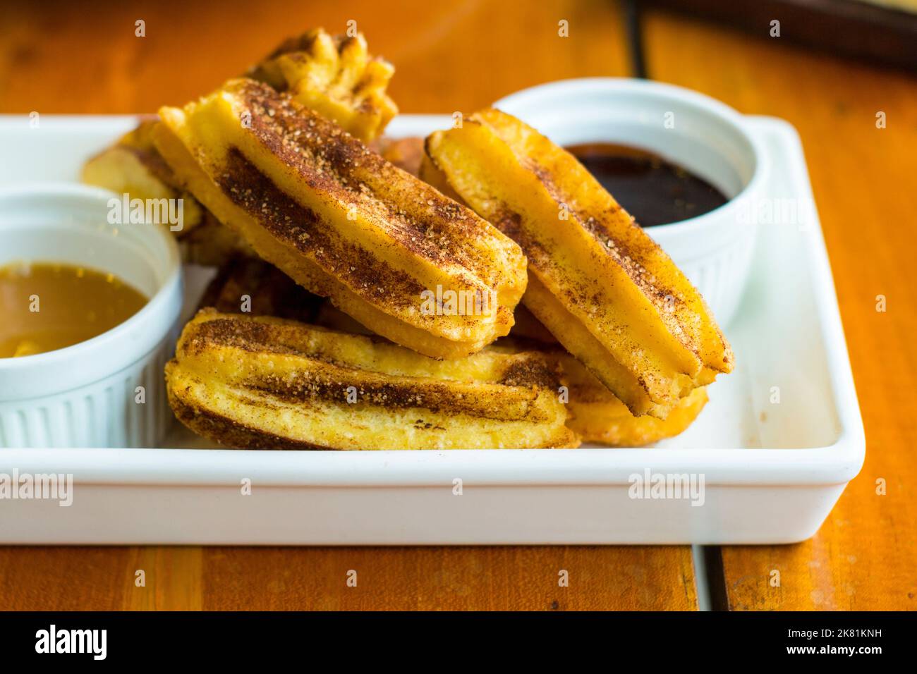 A dish of short churros with a caramel and chocolate dipping sauce in