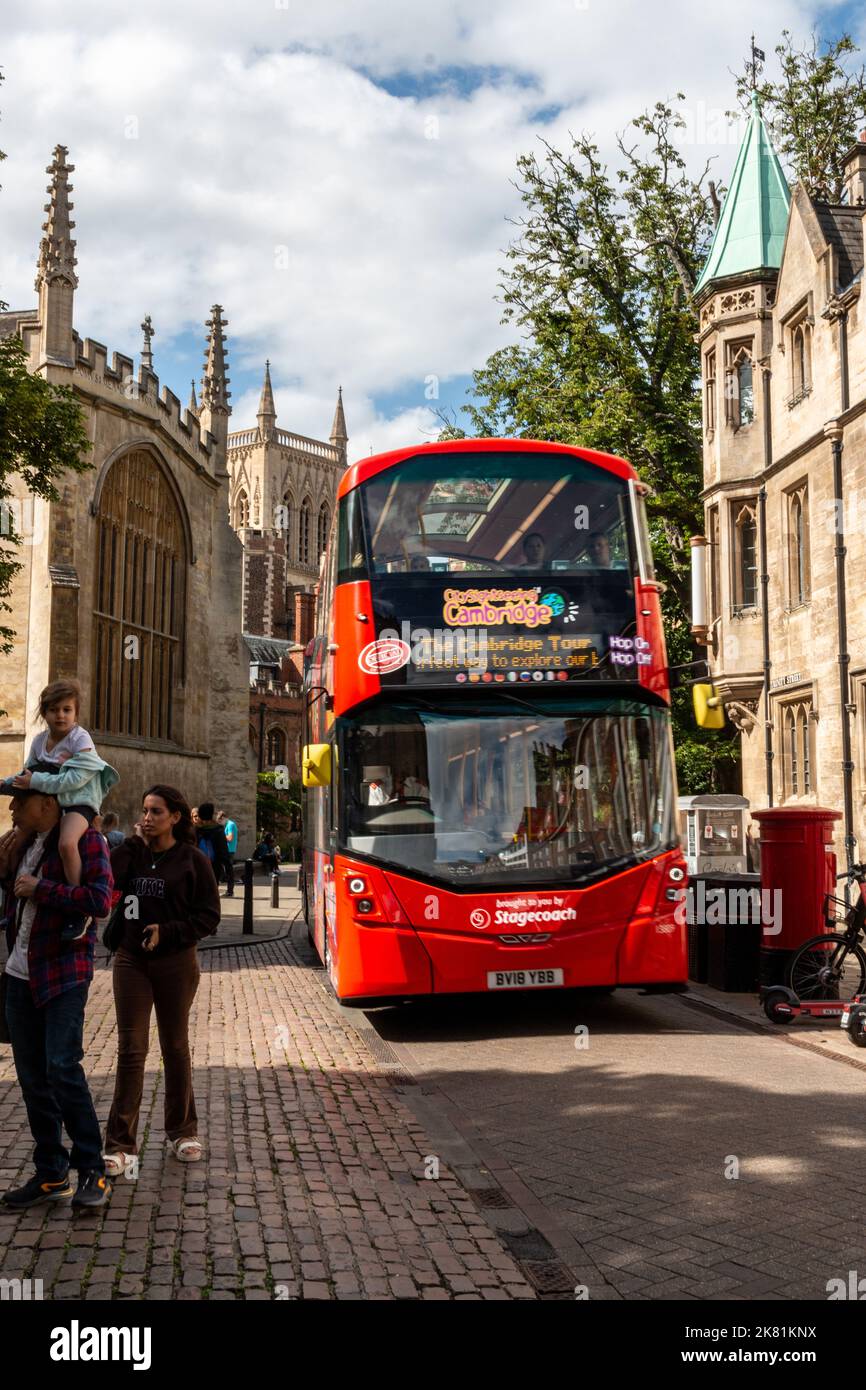 A red hop on hop off open top tour bus drives down Trinity Street in Cambridge, UK past St Johns College and Trinity College. Stock Photo
