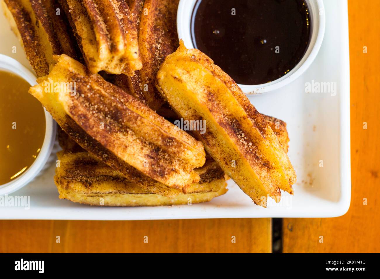 A dish of short churros with a caramel and chocolate dipping sauce in