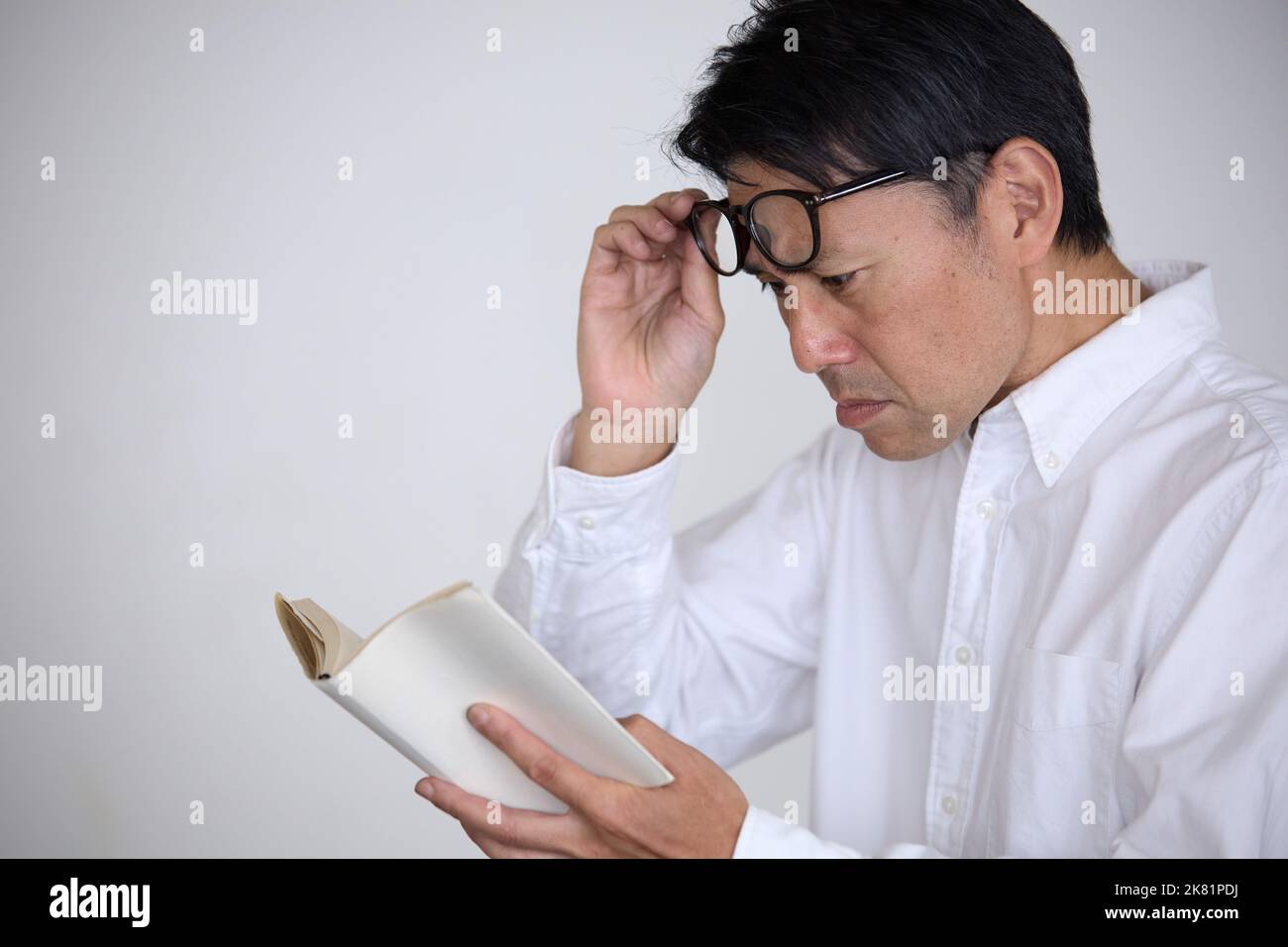Japanese man who has presbyopia finds difficulty in reading books Stock Photo