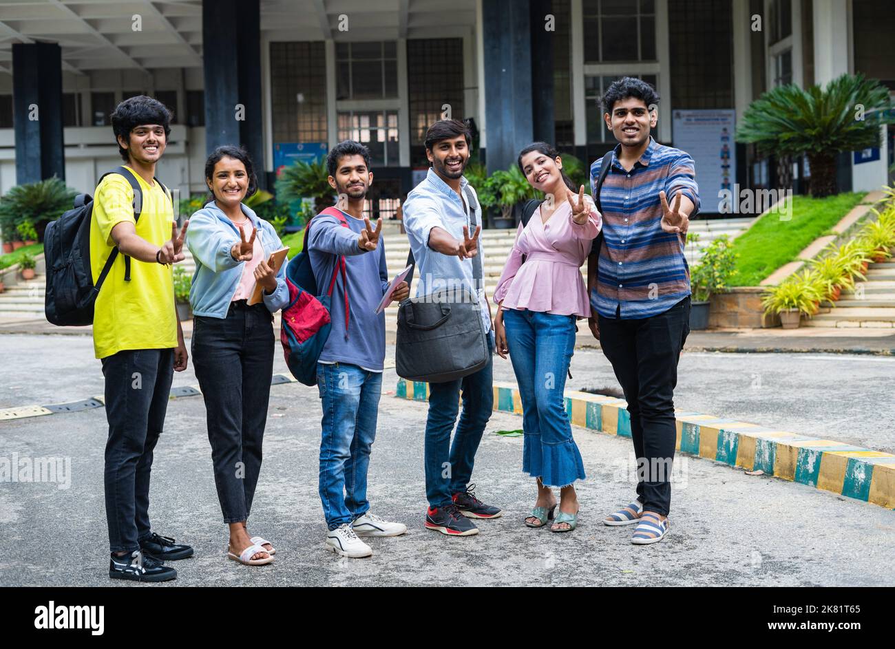full shot of confident students with backpack and books showing thumbs up by looking camera at college campus - concept of approval, education and Stock Photo