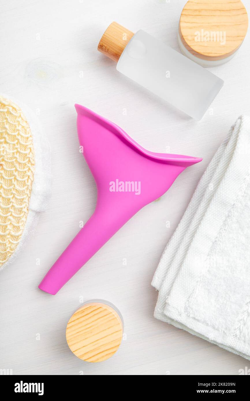 Device for women, pee funnel, tool that helps urinating standing. Pink silicone funnel between hygiene products. Flat lay view, studio shot. Stock Photo