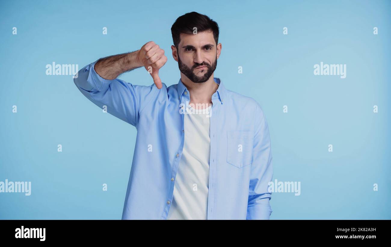 displeased bearded man in shirt showing thumb down isolated on blue Stock Photo