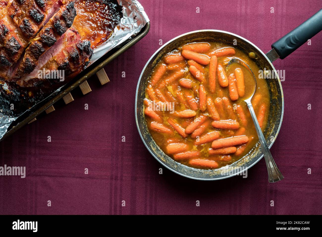 Sauteed carrots in a fry pan with a glazed smoked picnic ham in a pan
