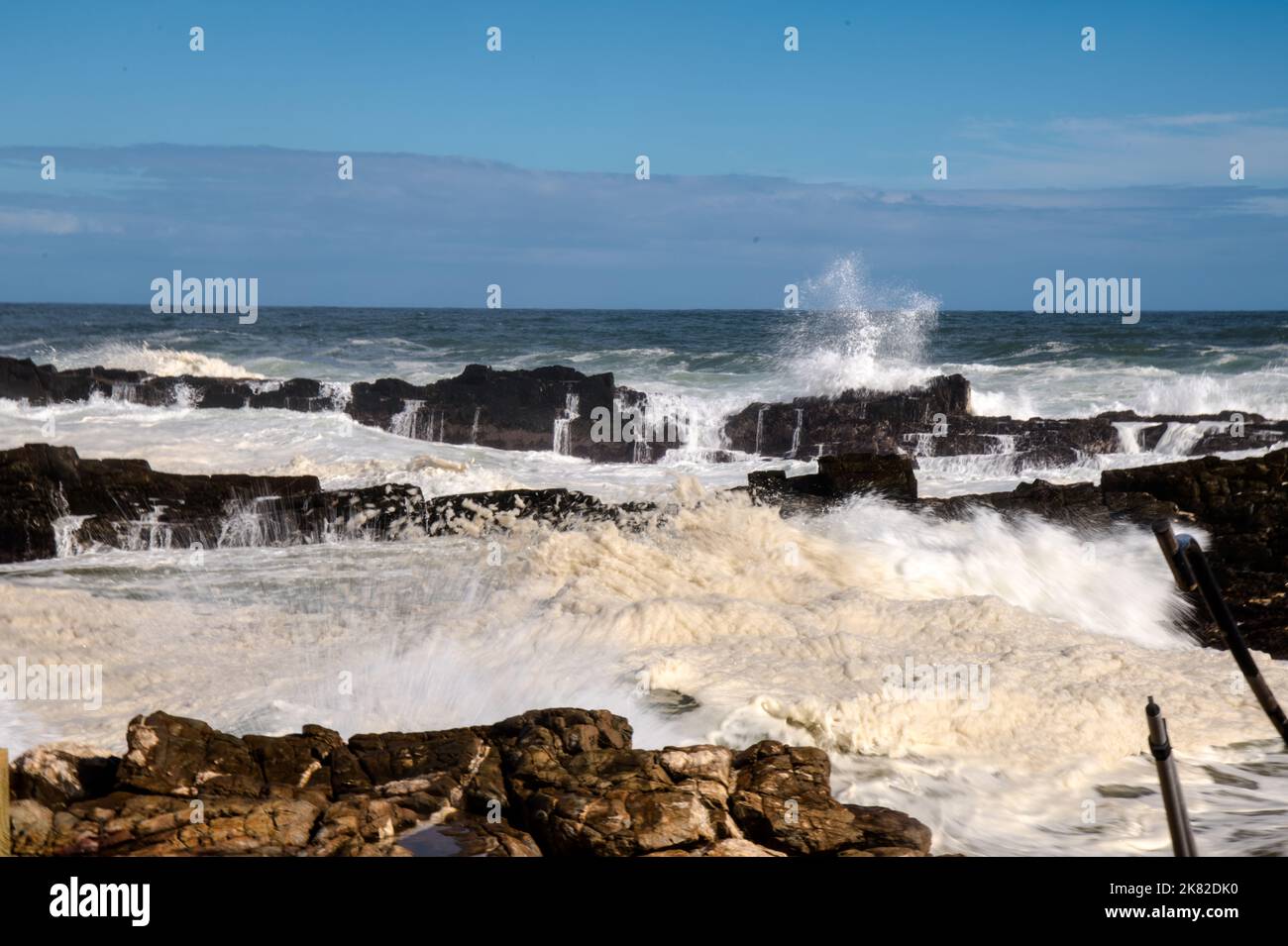 Crashing waves against jutting rocks on shoreline Stock Photo