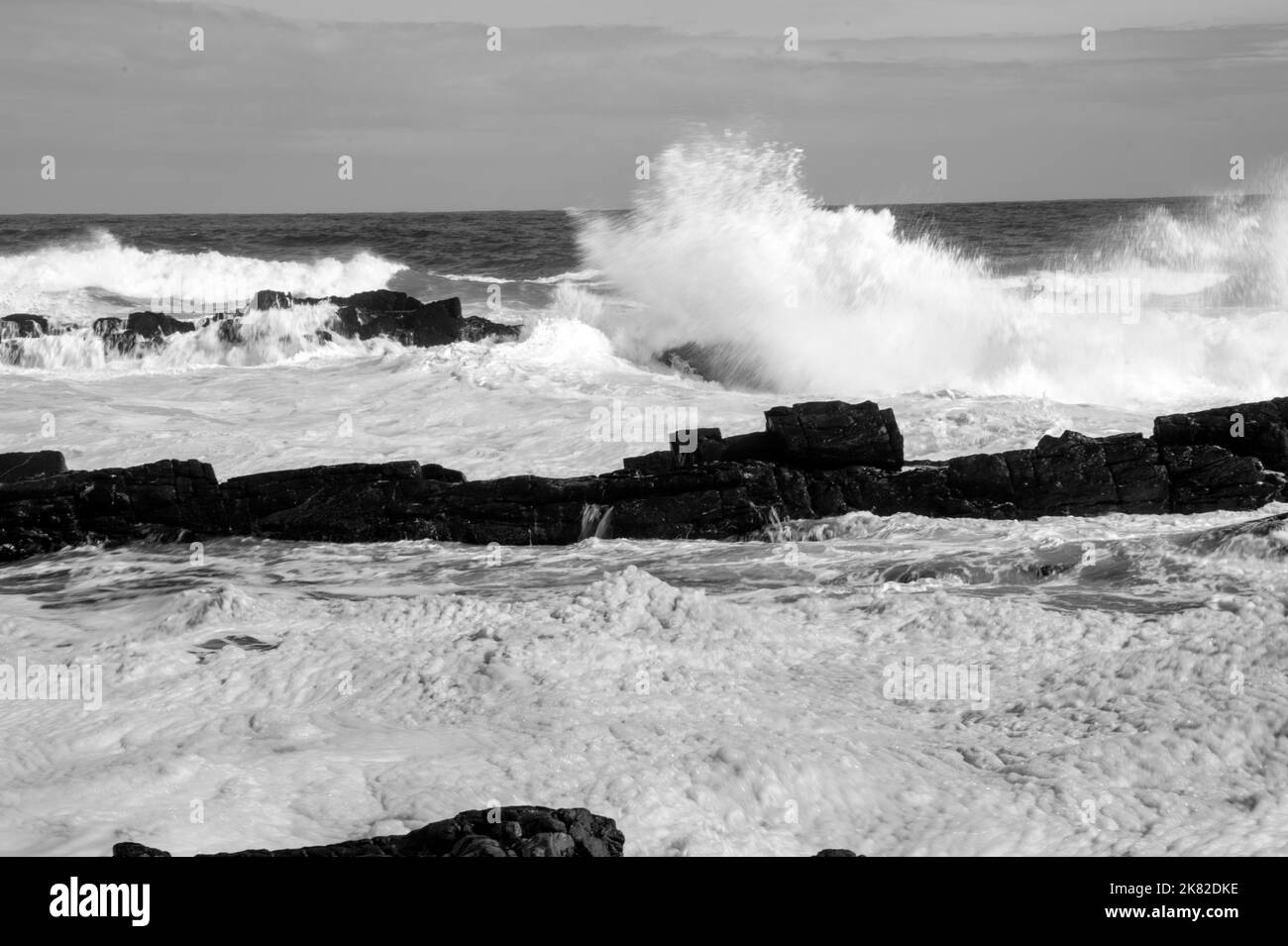 Crashing waves against jutting rocks on shoreline Stock Photo