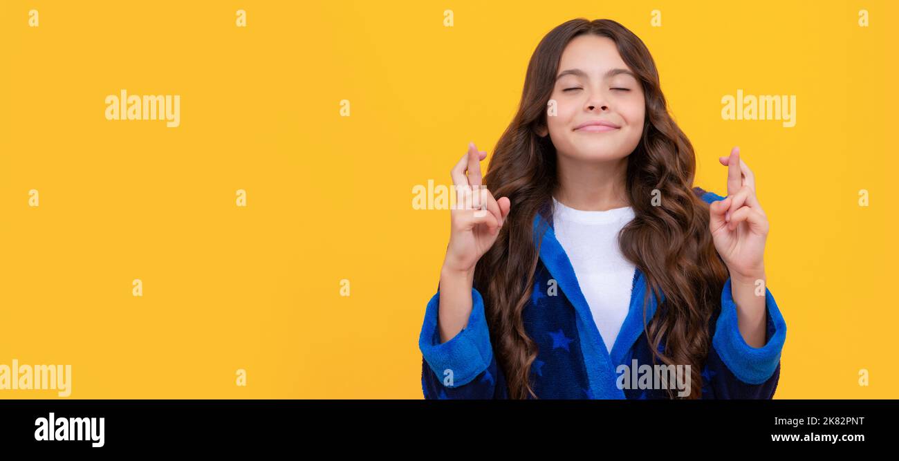 Superstitious girl with closed eyes keeping fingers crossed for luck yellow background, wish. Child face, horizontal poster, teenager girl isolated Stock Photo
