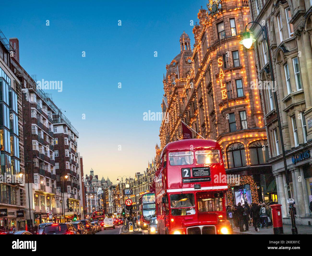 BROMPTON ROAD KNIGHTSBRIDGE WINTER SALES with vintage retro red routemaster tour bus and Harrods department store behind at dusk night with lit 'Sale' sign busy shoppers traffic Harrods Knightsbridge London SW1 Stock Photo