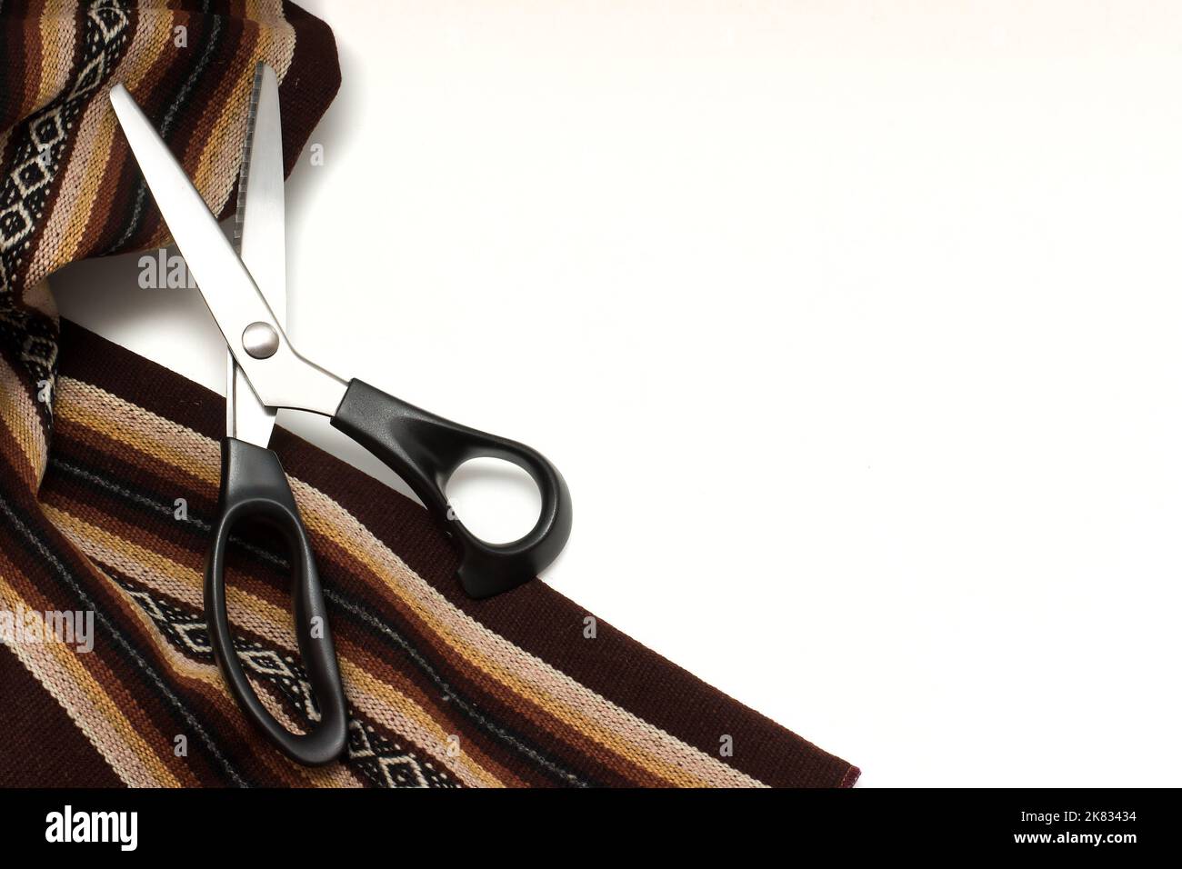 Thick brown patterned fabric and sewing scissors  isolated on white background. Stock Photo