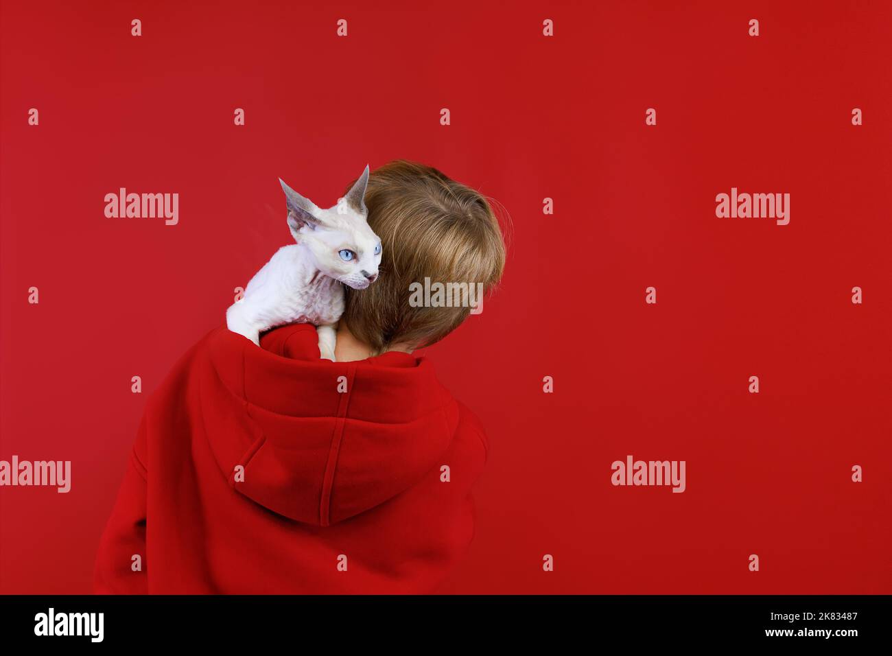 a boy in a red suit stands with his back and a small cat sits in his hood Stock Photo