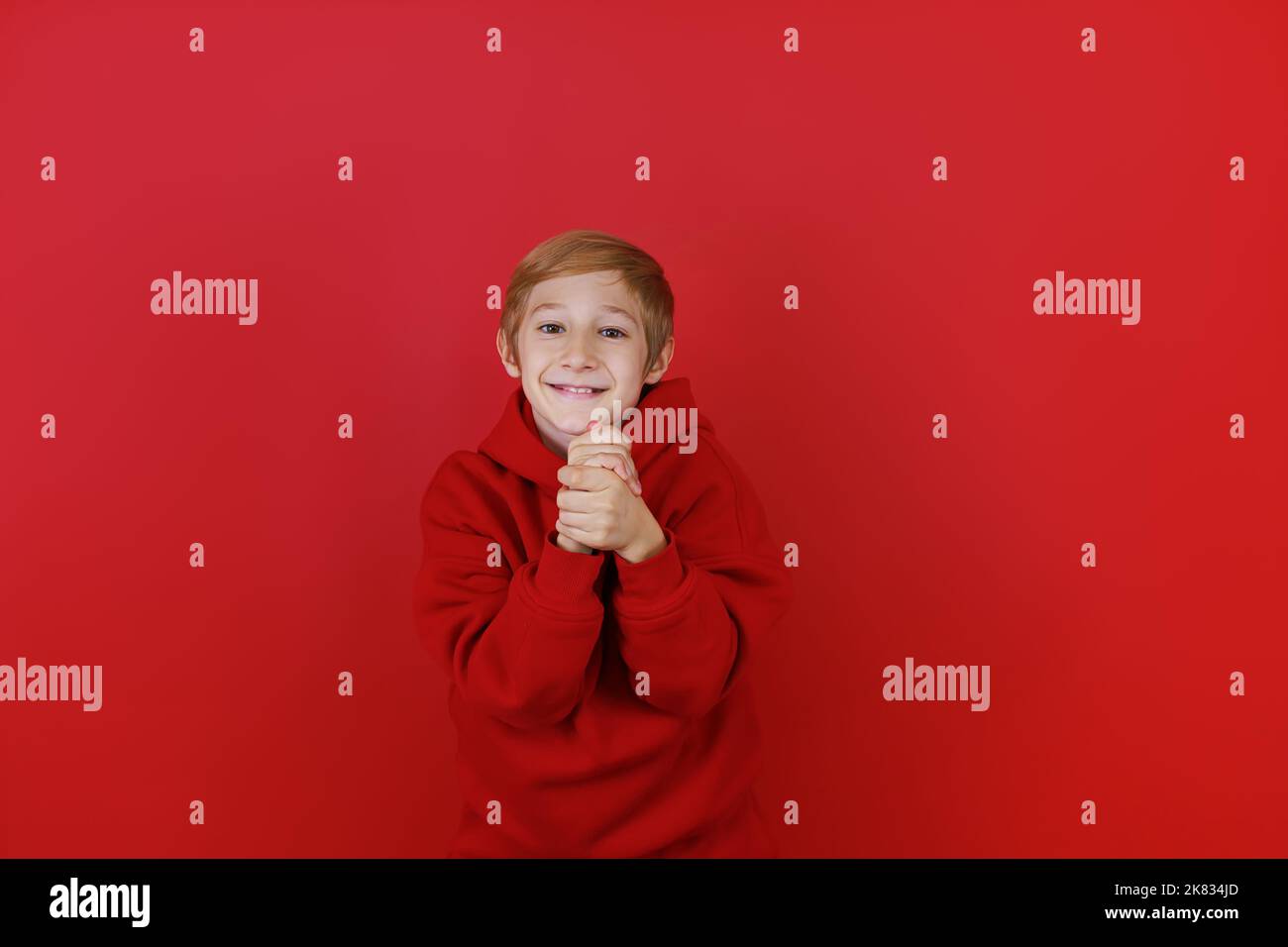 a boy in a red suit and on a red background folded his hands in front of him Stock Photo