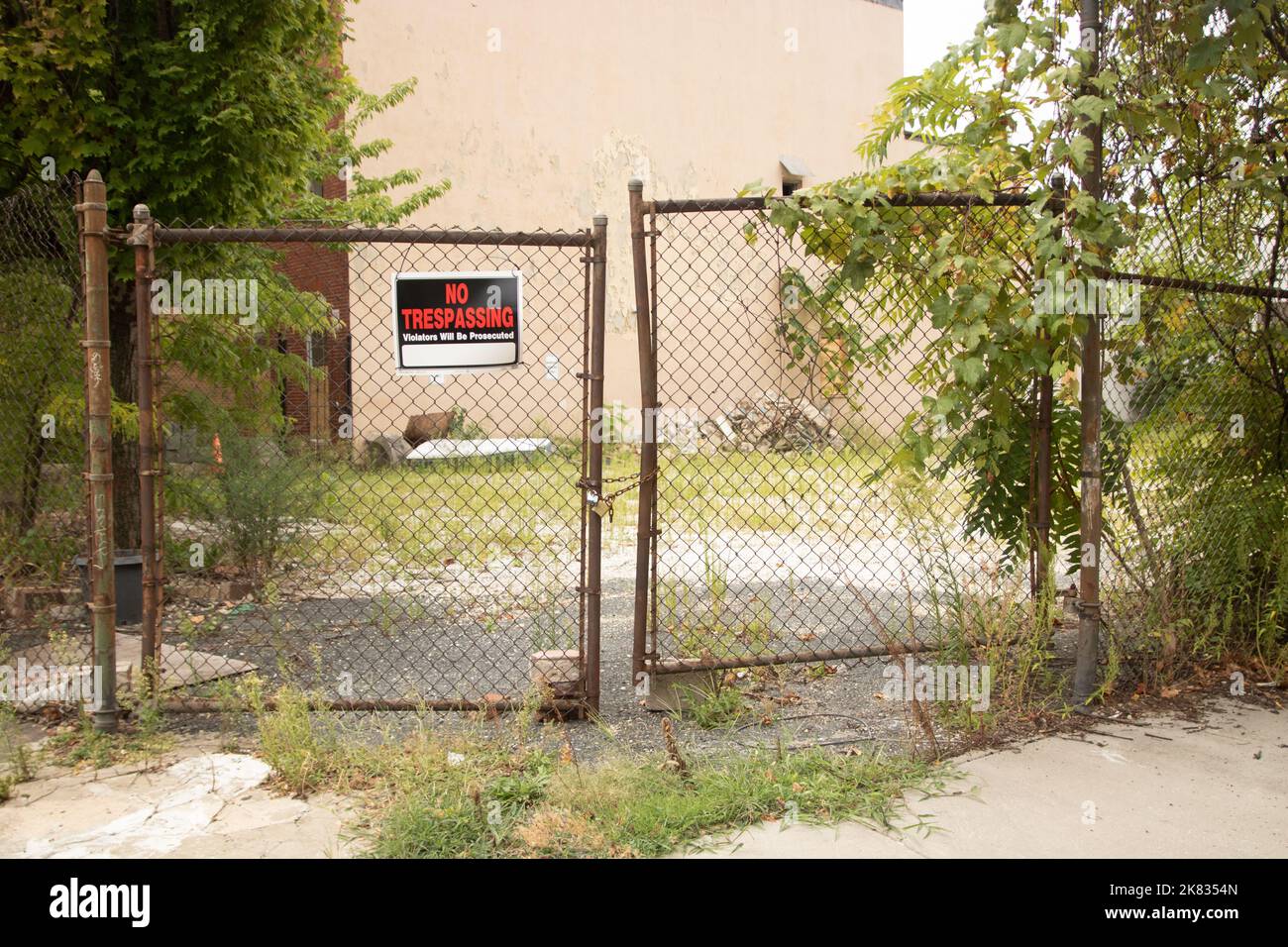 No trespassing sign with old chain link fence with overgrown lot Stock Photo