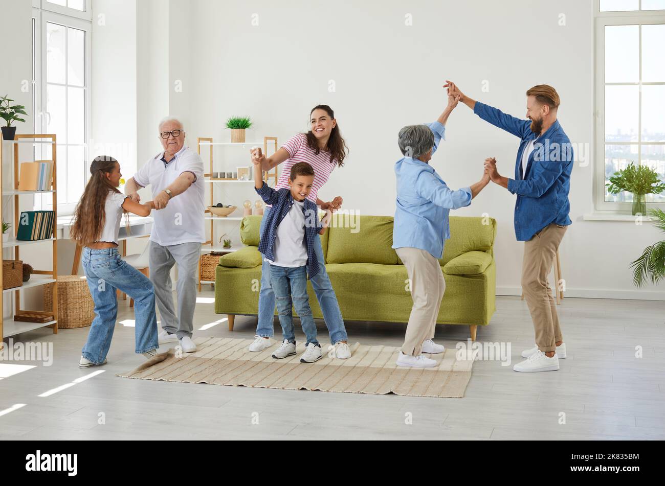Family members of different generations having fun listening music and dancing in room at home. Stock Photo