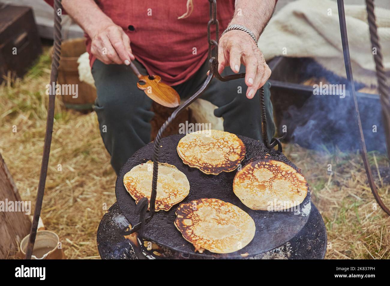 Old man frying pancakes in a pan on a campfire Stock Photo