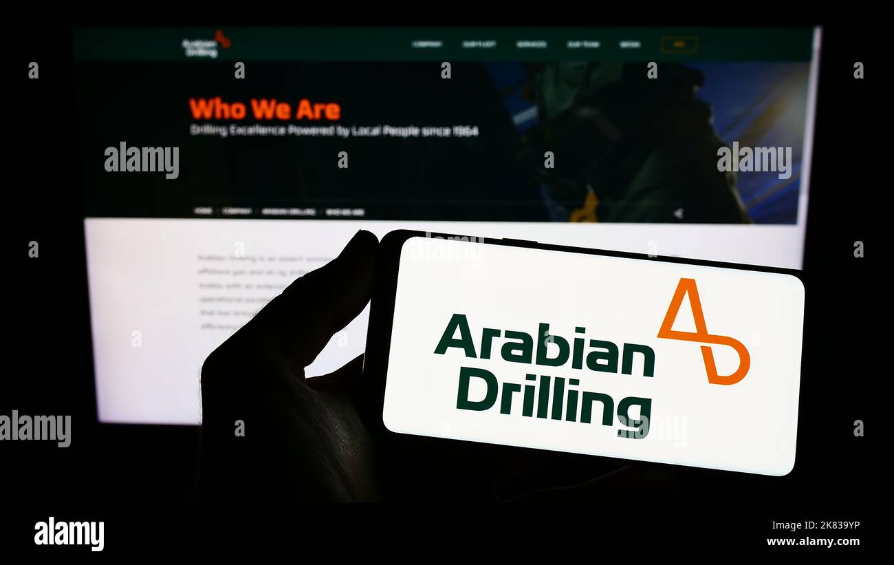 Person holding smartphone with logo of Saudi business Arabian Drilling Company (ADC) on screen in front of website. Focus on phone display. Stock Photo