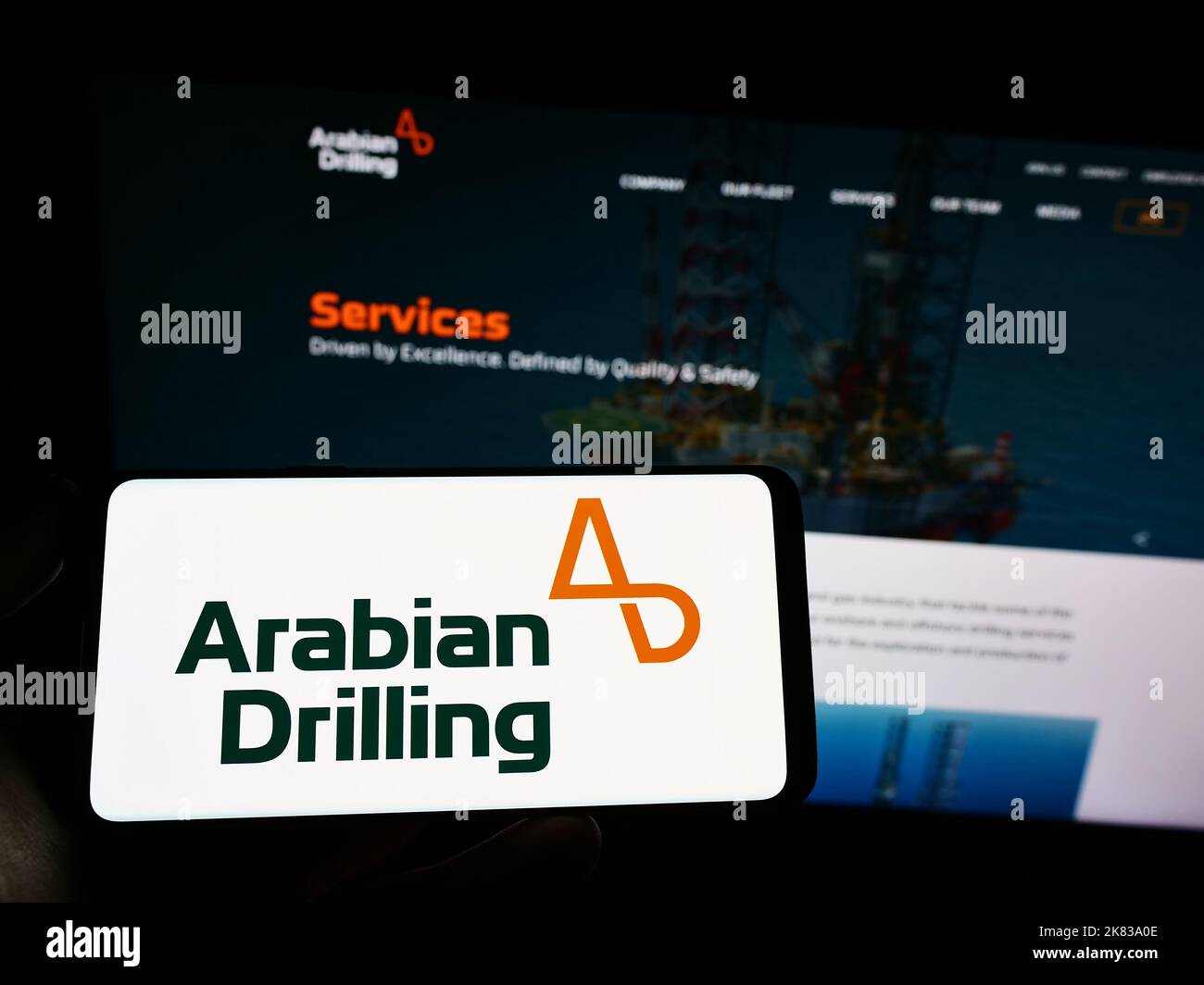 Person holding cellphone with logo of Saudi business Arabian Drilling Company (ADC) on screen in front of webpage. Focus on phone display. Stock Photo