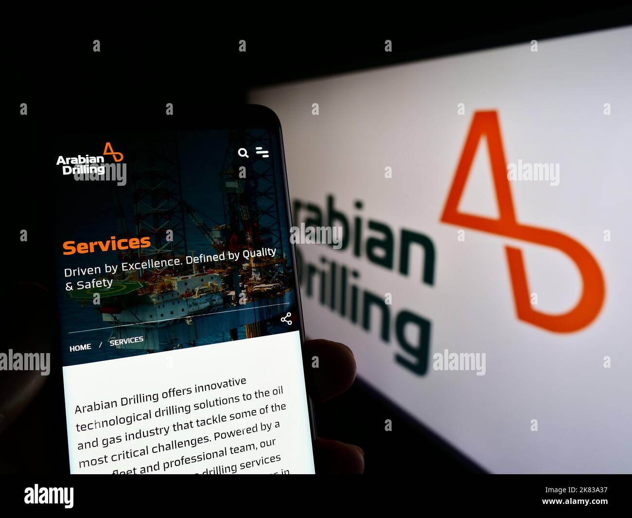 Person holding cellphone with webpage of Saudi business Arabian Drilling Company (ADC) on screen with logo. Focus on center of phone display. Stock Photo