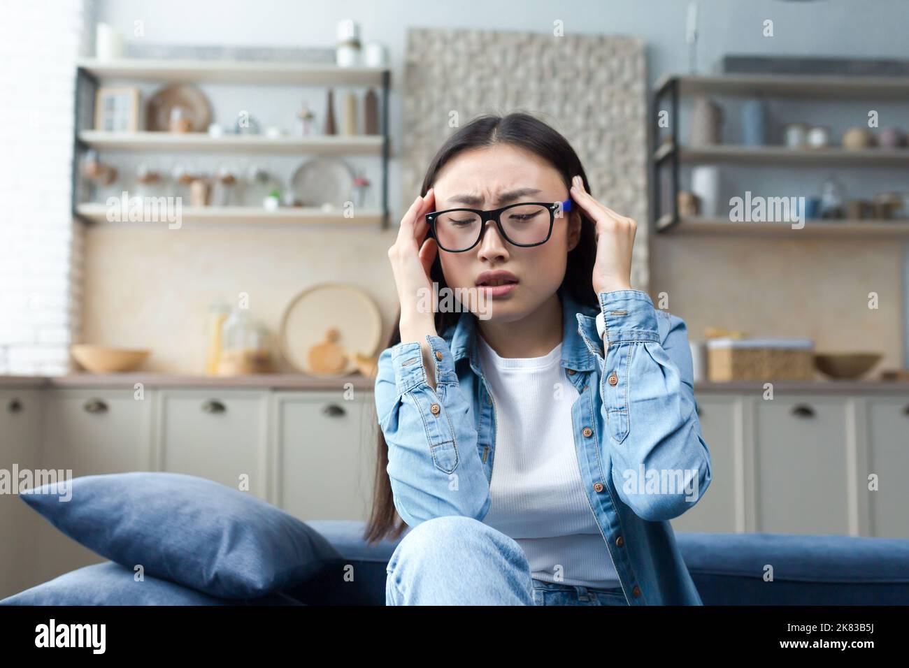 Headache, exhaustion. A young beautiful Asian woman holds her head