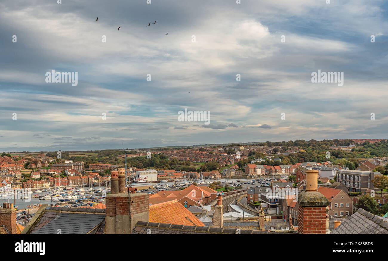 A view over the rooftops of Whitby. A harbour is in the distance and ...