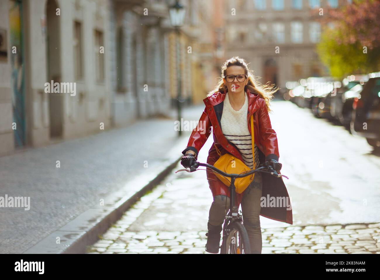 stylish 40 years old woman in red rain coat outdoors on the city street ...