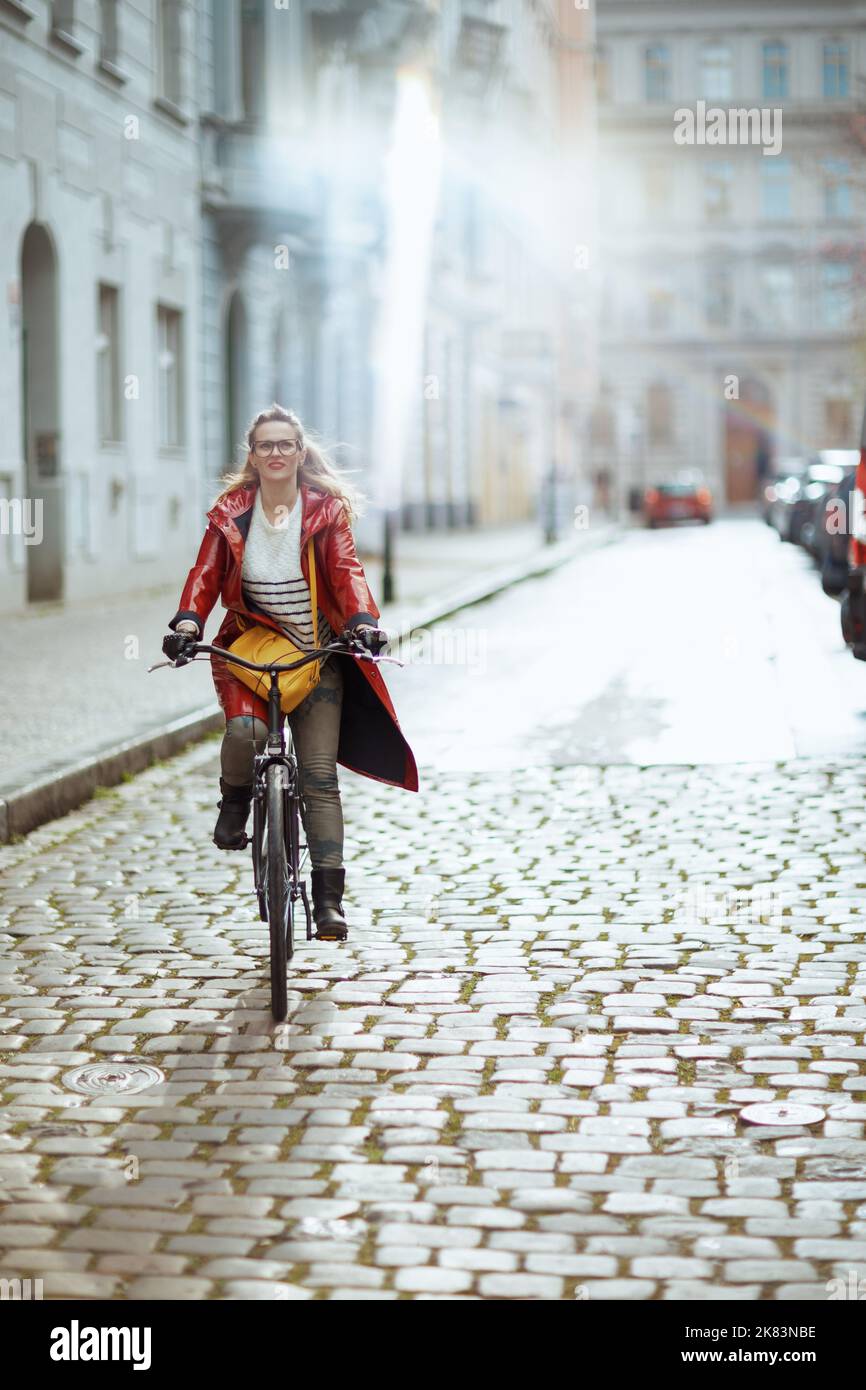 modern middle aged woman in red rain coat outside in the city riding ...