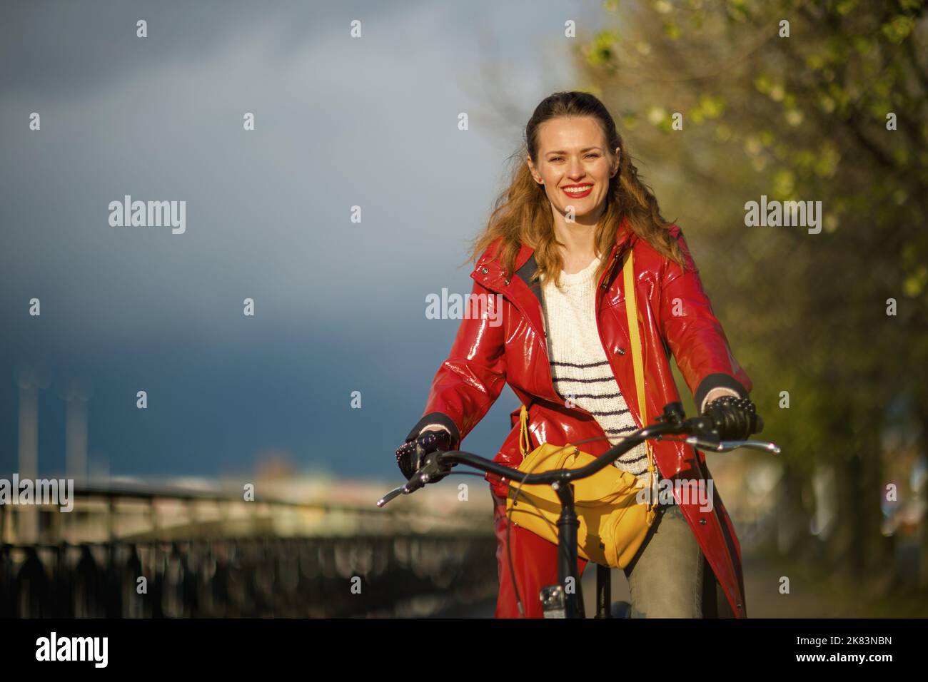 smiling elegant 40 years old woman in red rain coat outside on the city ...