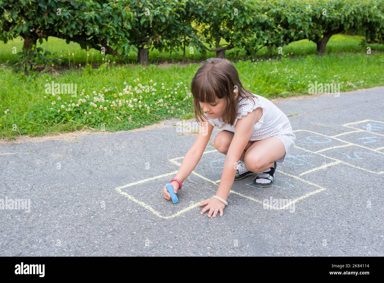 A little cute schoolgirl draws a colorful chalk on the sidewalk Stock Photo