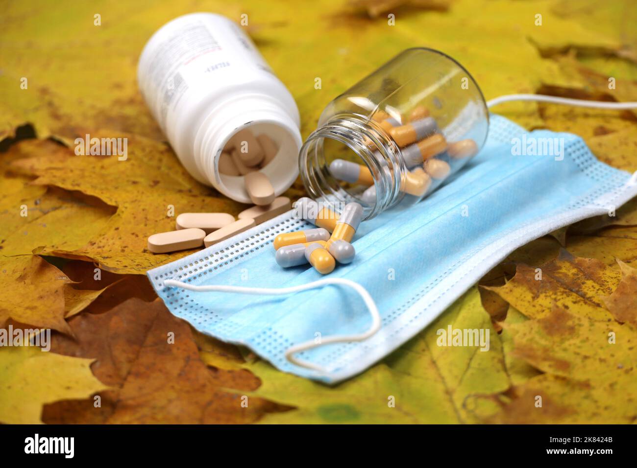 Pills on autumn maple leaves, bottles with scattered capsules on medical face mask. Pharmacy, antidepressants, coronavirus treatment Stock Photo