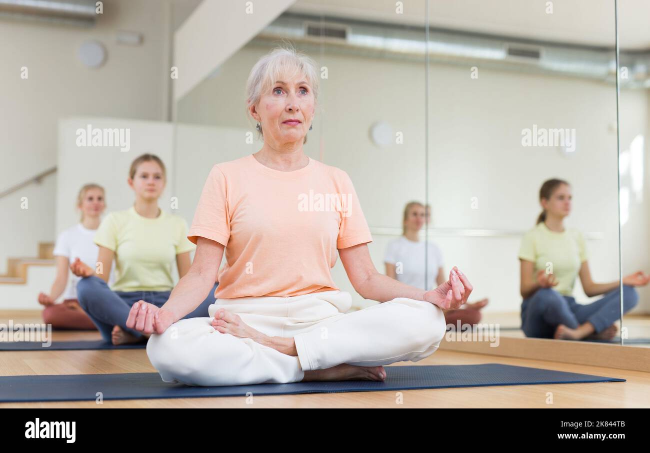 Senior woman sitting on mat in lotus pose during yoga training Stock ...