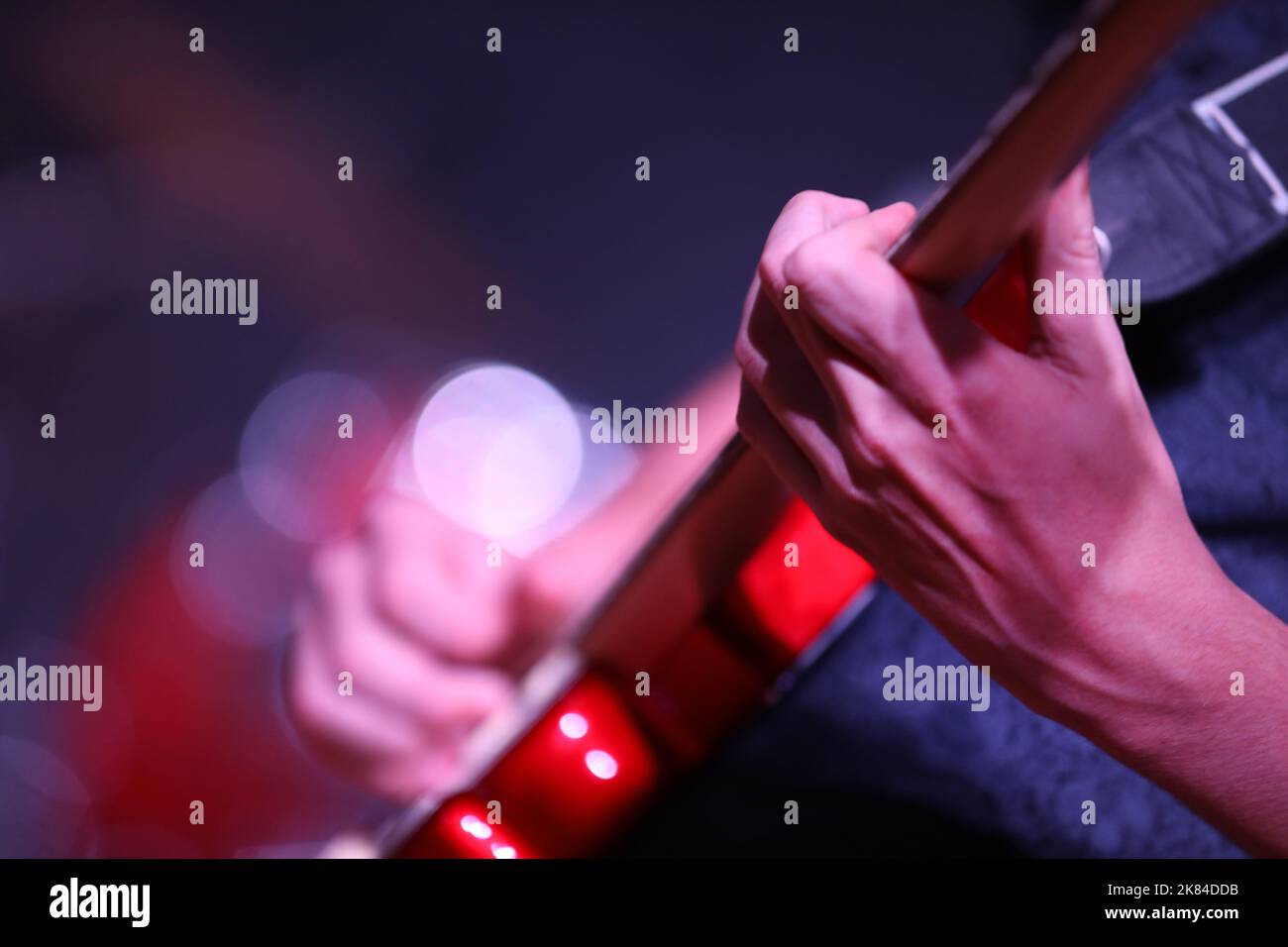 Close up of hand and fingers playing music on a bright red electric guitar. Hand strumming fret with a deliberately blurred spotlight background Stock Photo