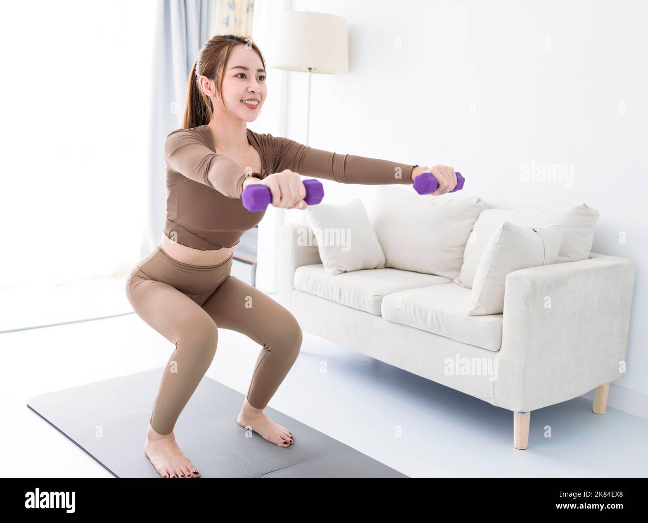 Young woman with dumbbells exercising at home Stock Photo