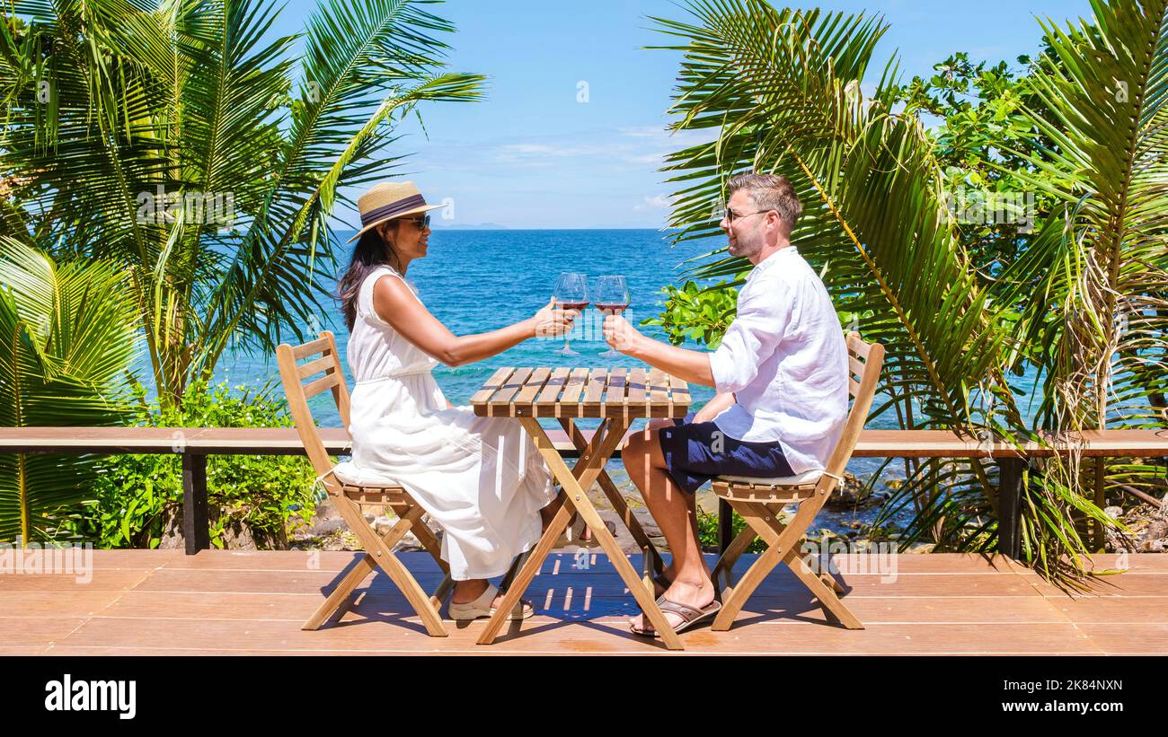 couple drinking wine at ocean front during sunset, men and women on the ...