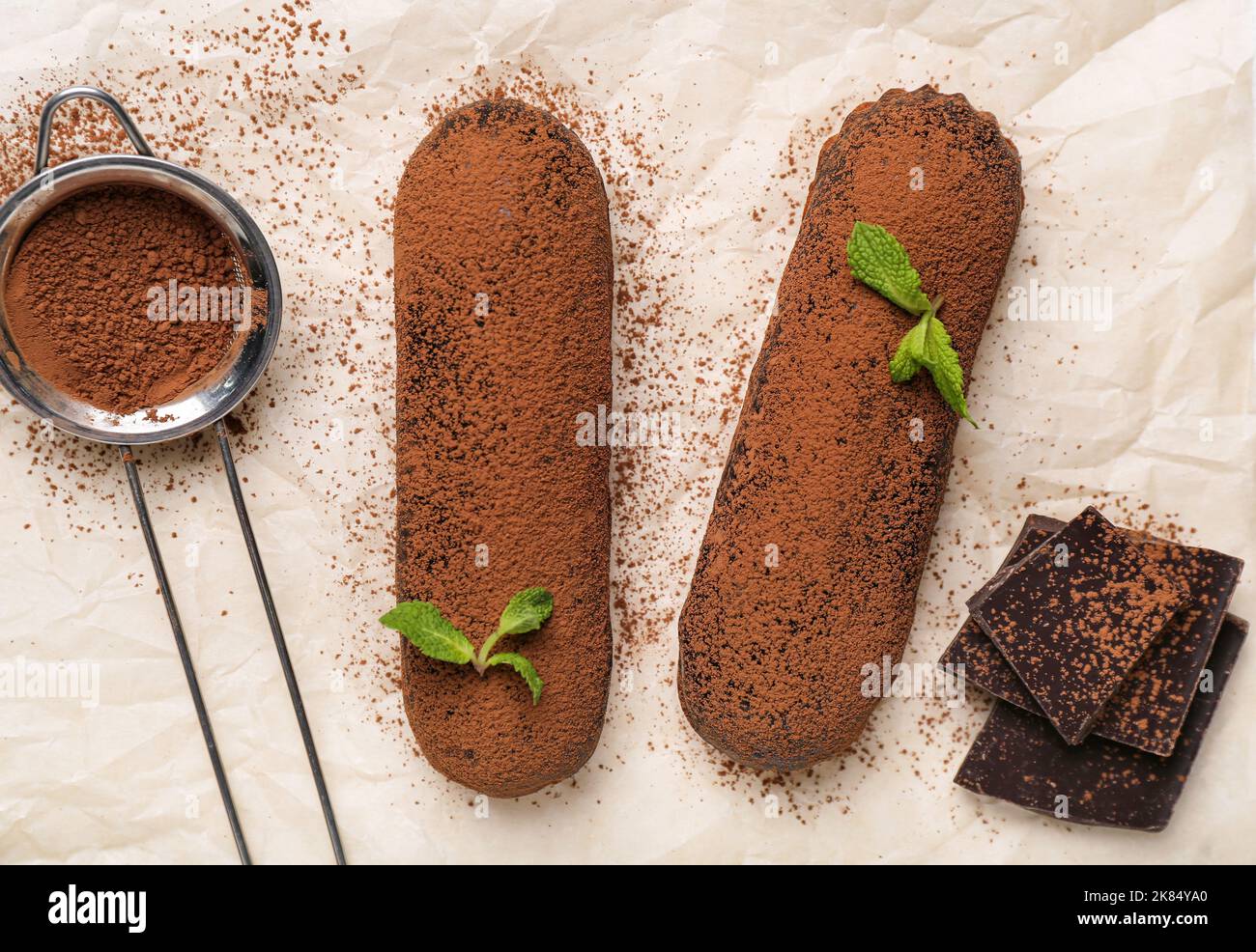 Baking paper with tasty chocolate eclairs and cocoa powder, closeup